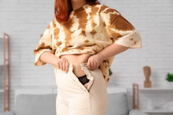 Image of woman trying to do her trousers up after pregnancy weight gain Braintree