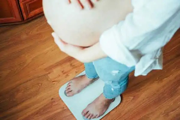 Image of woman weighing herself and experiencing weight gain through pregnancy Braintree